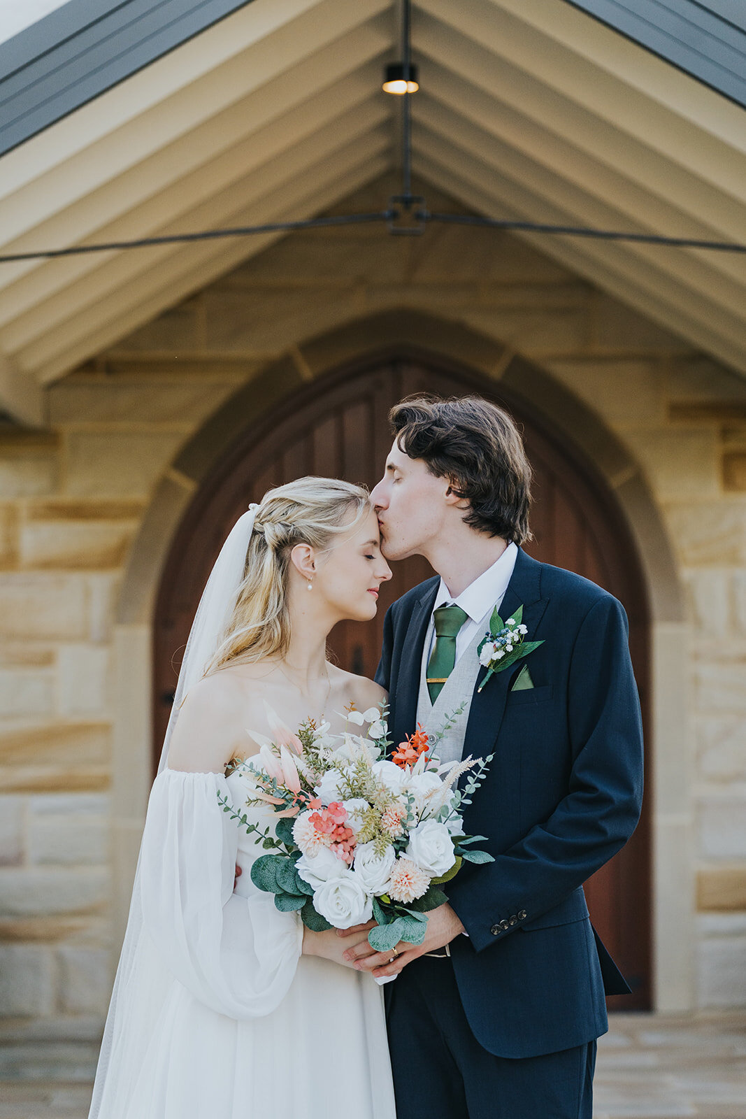 Groom kissing the bride outside a sandstone chapel