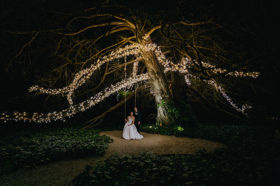 Couple on a swing beneath a tree wrapped in fairy lights
