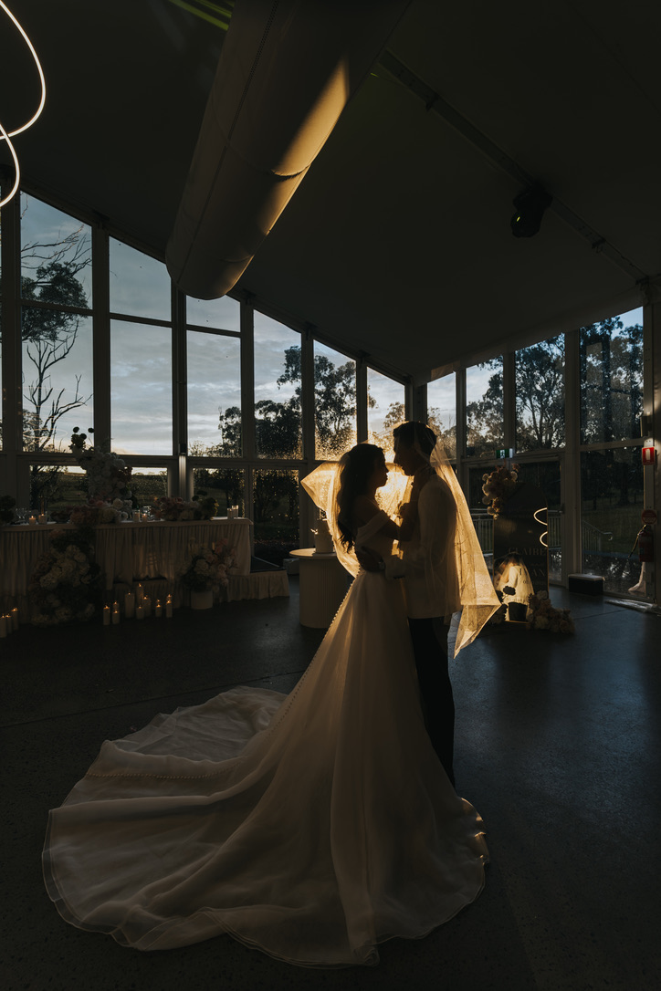 Couple silhouetted under the veil at dusk in a glass venue
