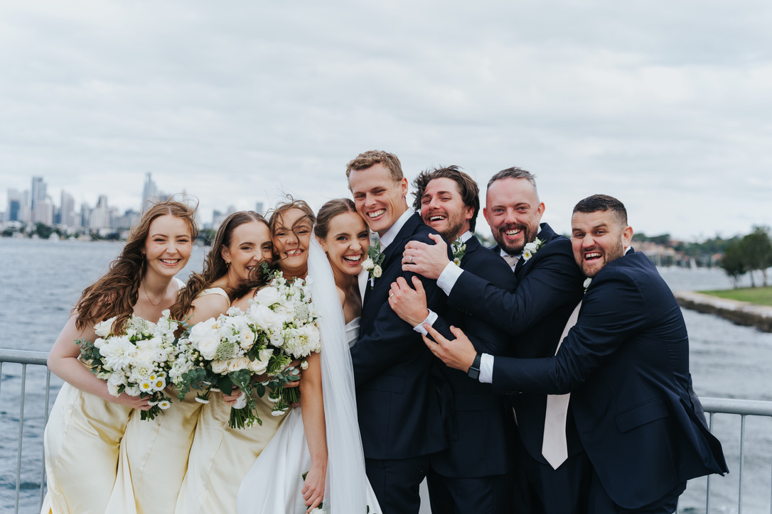 Bride, groom and bridal party laughing together by the harbour
